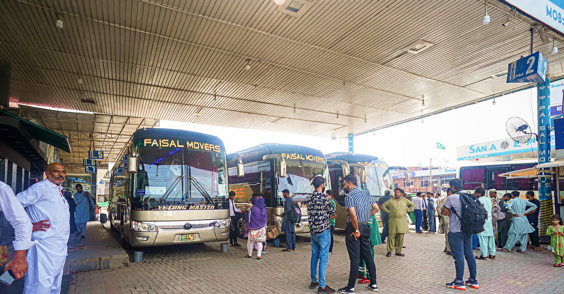 Real Faisal Movers Yutong Master buses lined up at a terminal in Pakistan with passengers boarding