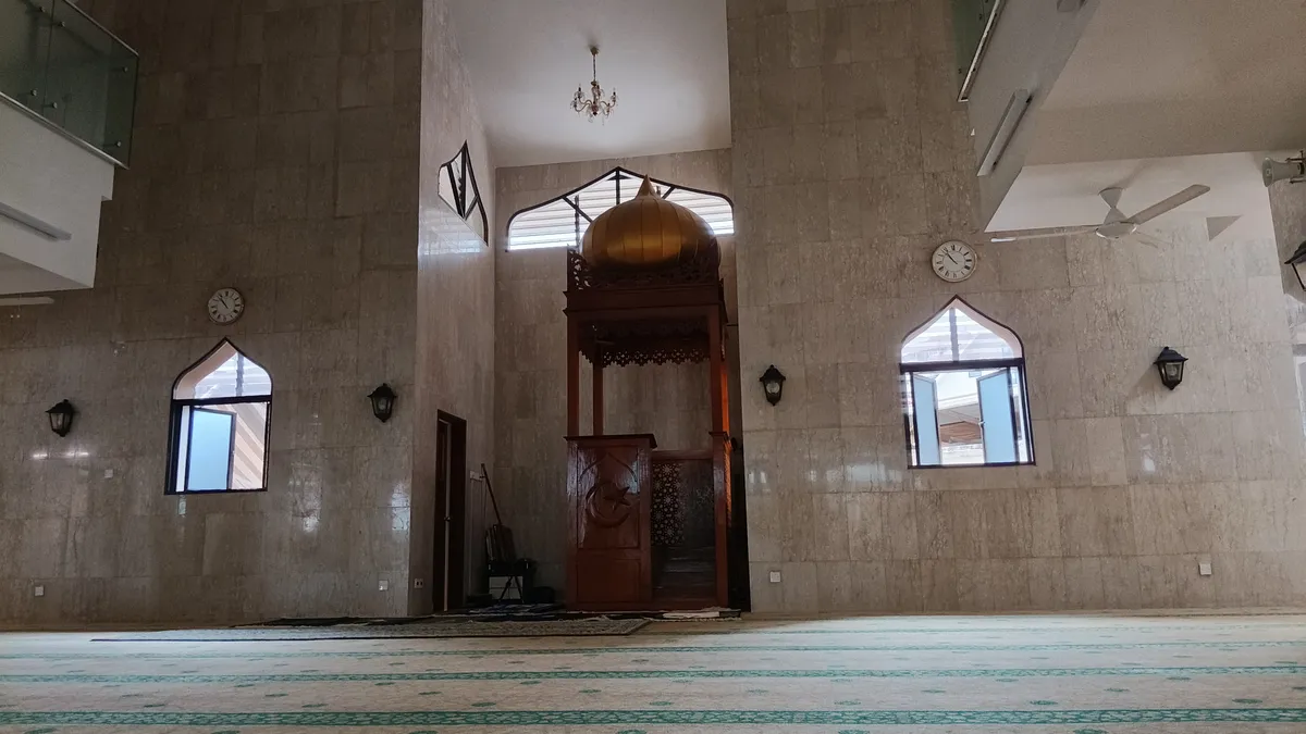 Photograph of a spacious mosque prayer hall with rows of patterned prayer carpet